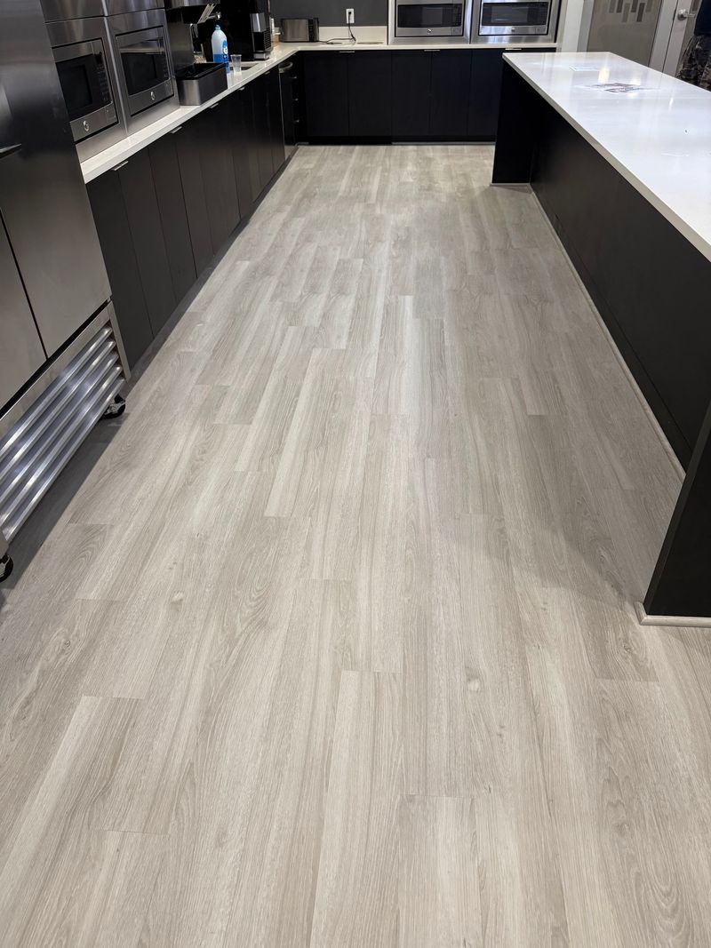 Long kitchen aisle finished with light gray wood-look plank flooring