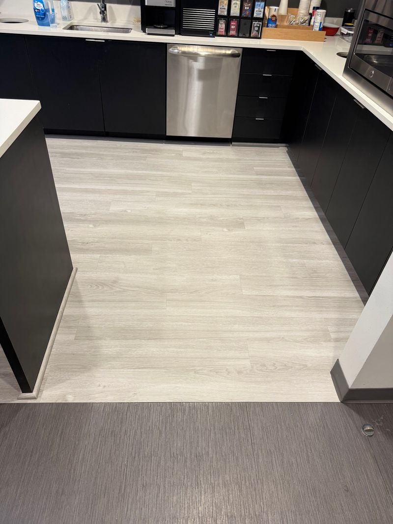 Coffee station aisle with light gray wood-look planks bordered by carpet tile