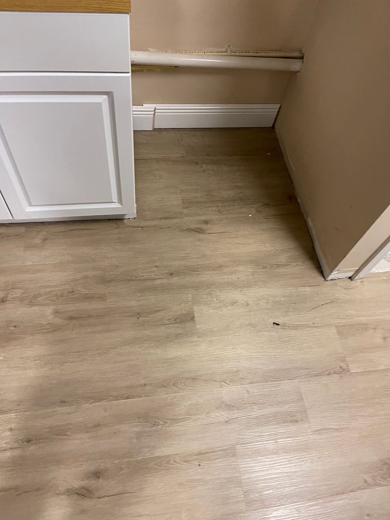 Empty office corner with light gray wood-look plank flooring and baseboards