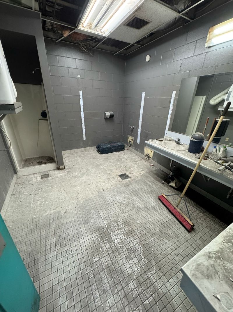 Commercial restroom with mosaic tile being chipped up and dust across floor