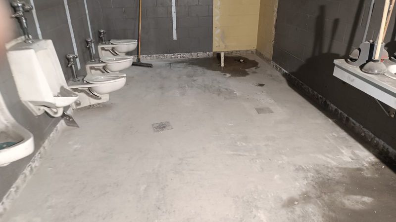 Commercial restroom stripped down to bare concrete slab after tile removal