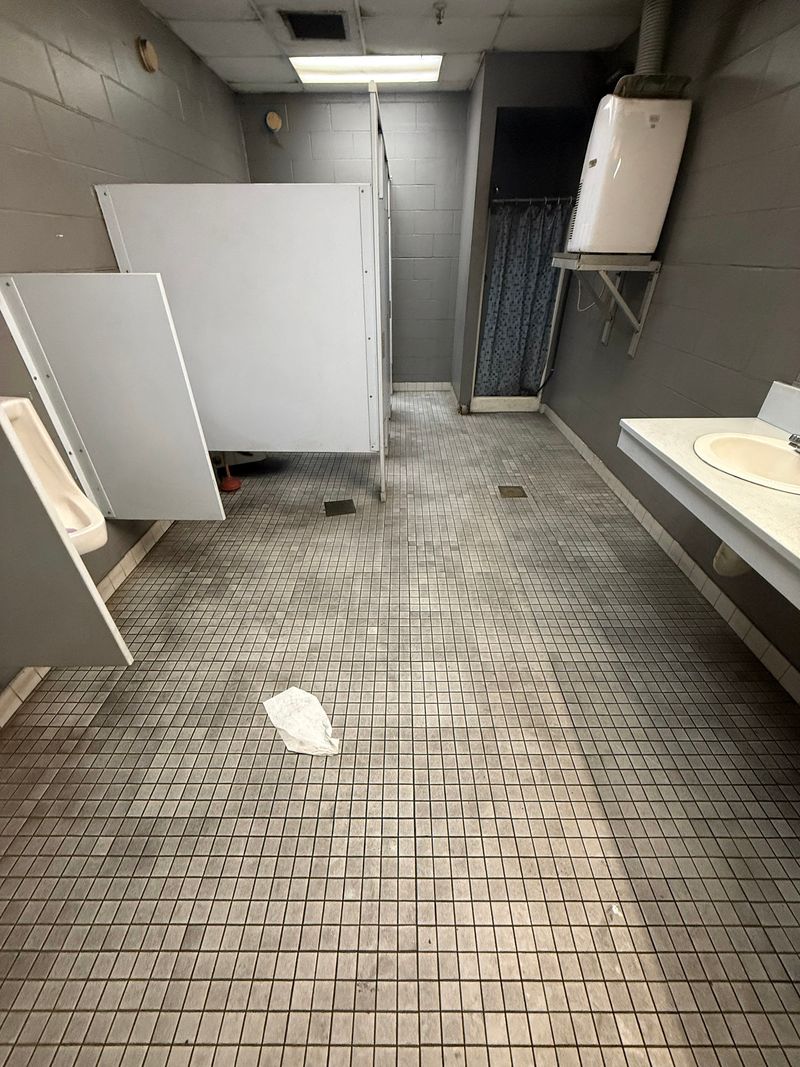 Commercial restroom with worn small gray mosaic tile floor before removal