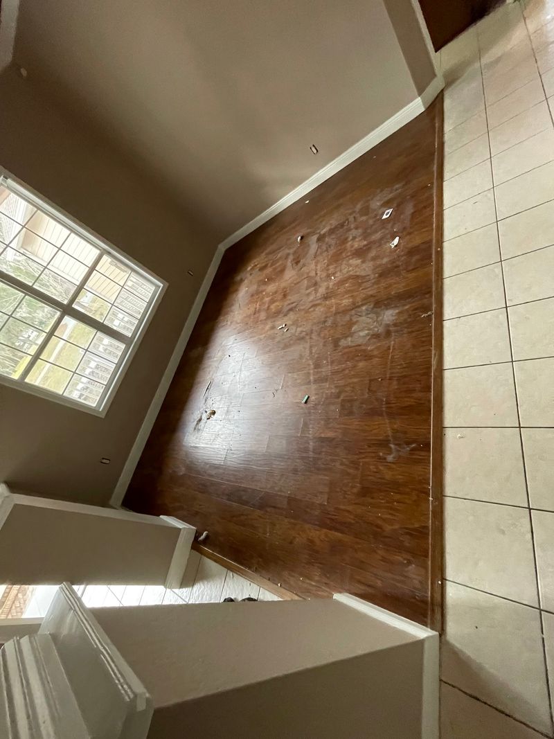 Bedroom with worn dark wood-look plank floor next to a beige tile hallway