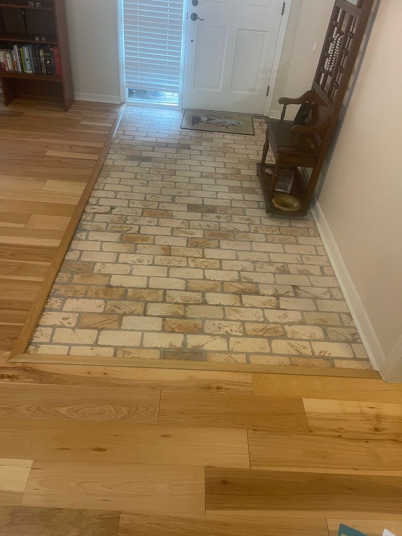 Front entry with light natural hardwood planks bordering a brick paver section