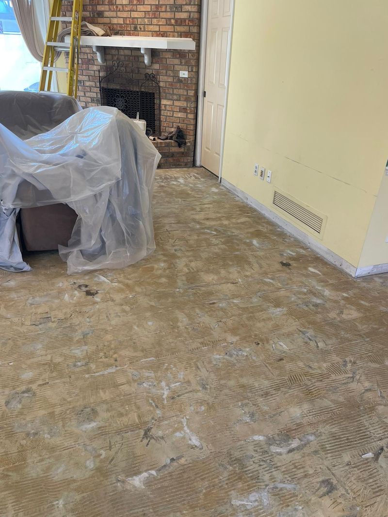 Living room slab scraped clean after flooring removal, brick fireplace behind
