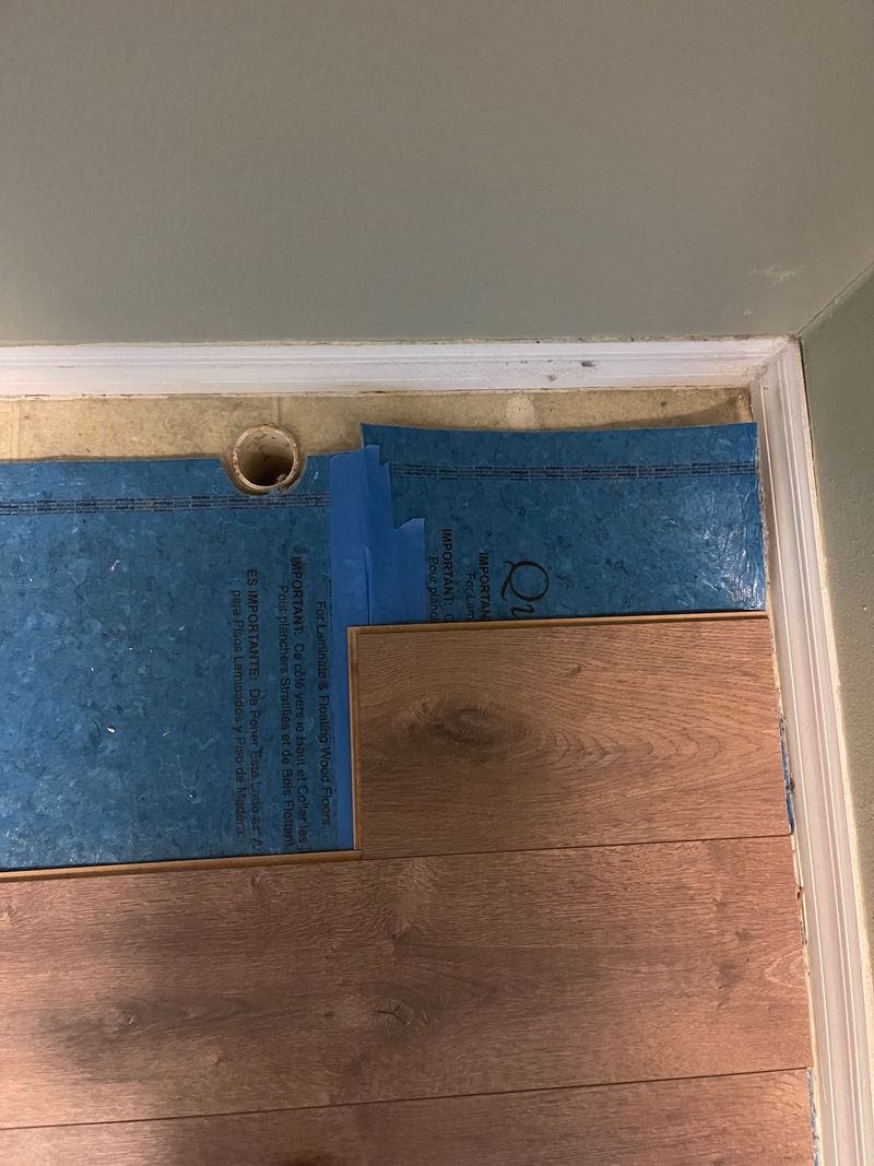 Brown laminate planks going down over blue underlayment in a bedroom