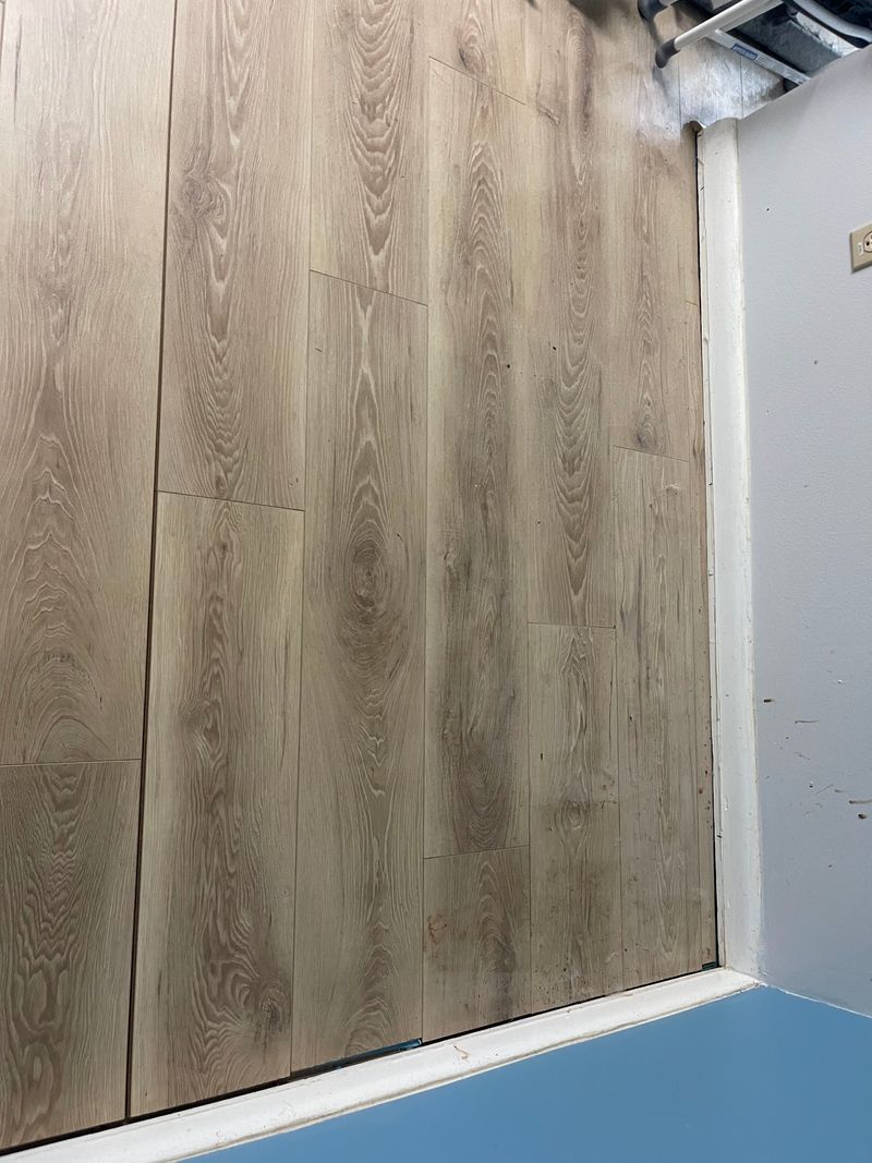 Close-up of light oak laminate planks meeting a white baseboard