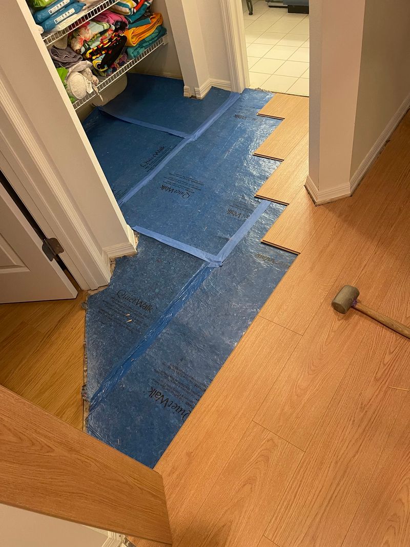 Light oak-look laminate planks going in over blue underlayment near a pantry