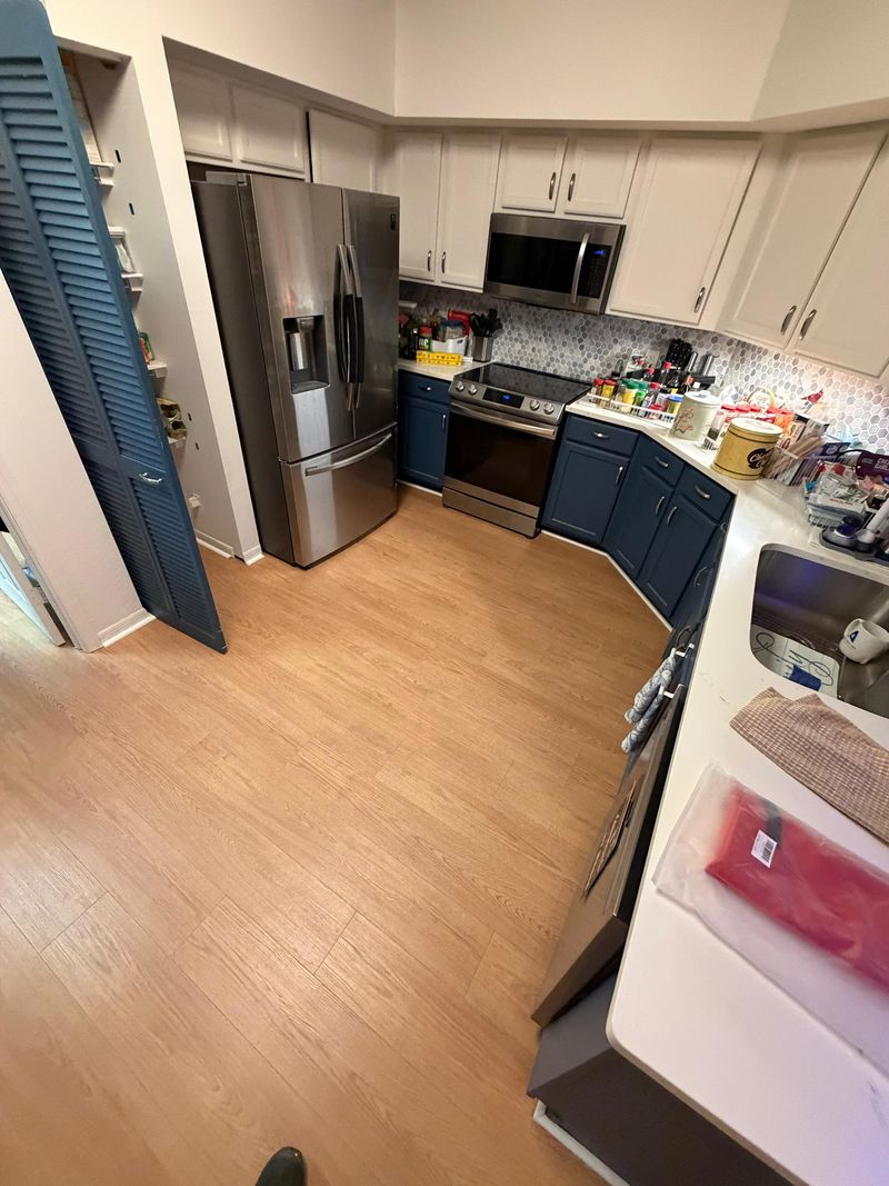Kitchen with light oak-look laminate flooring, navy lower cabinets and white uppers
