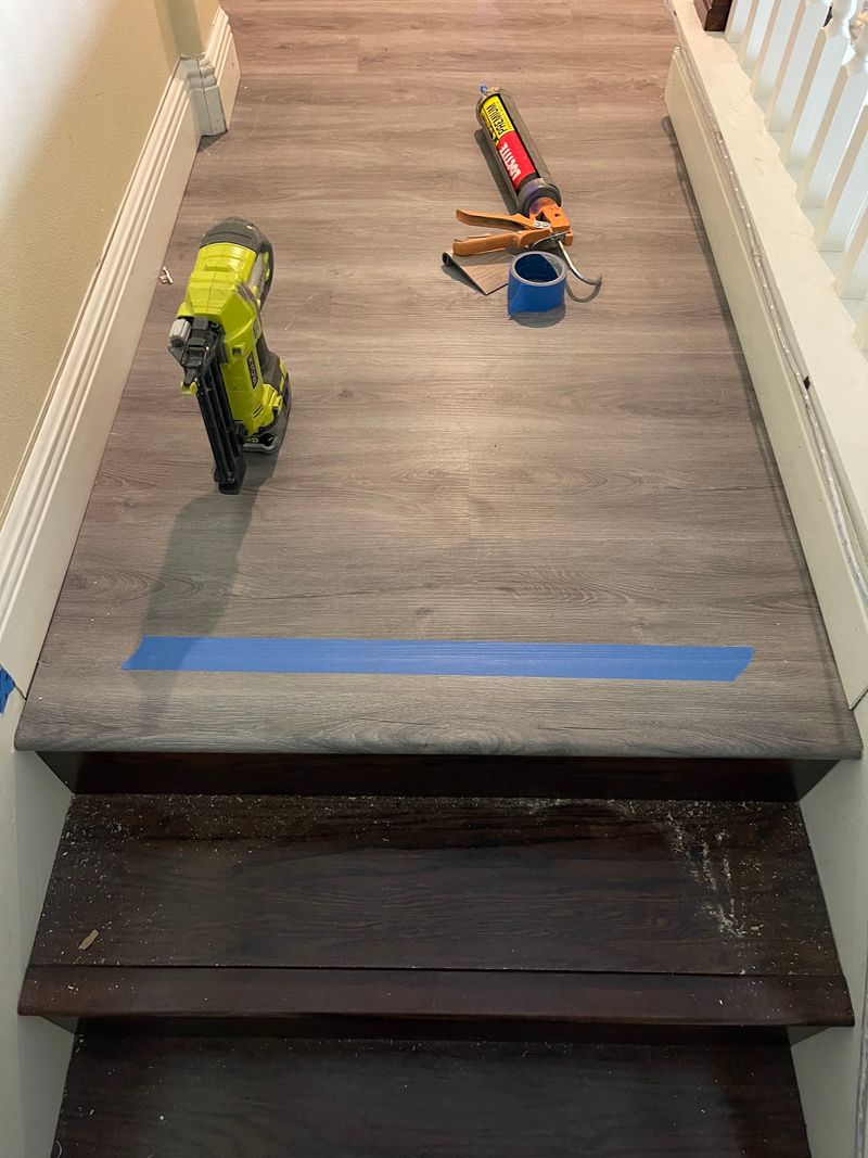 Top stair landing covered in gray vinyl plank above old dark treads