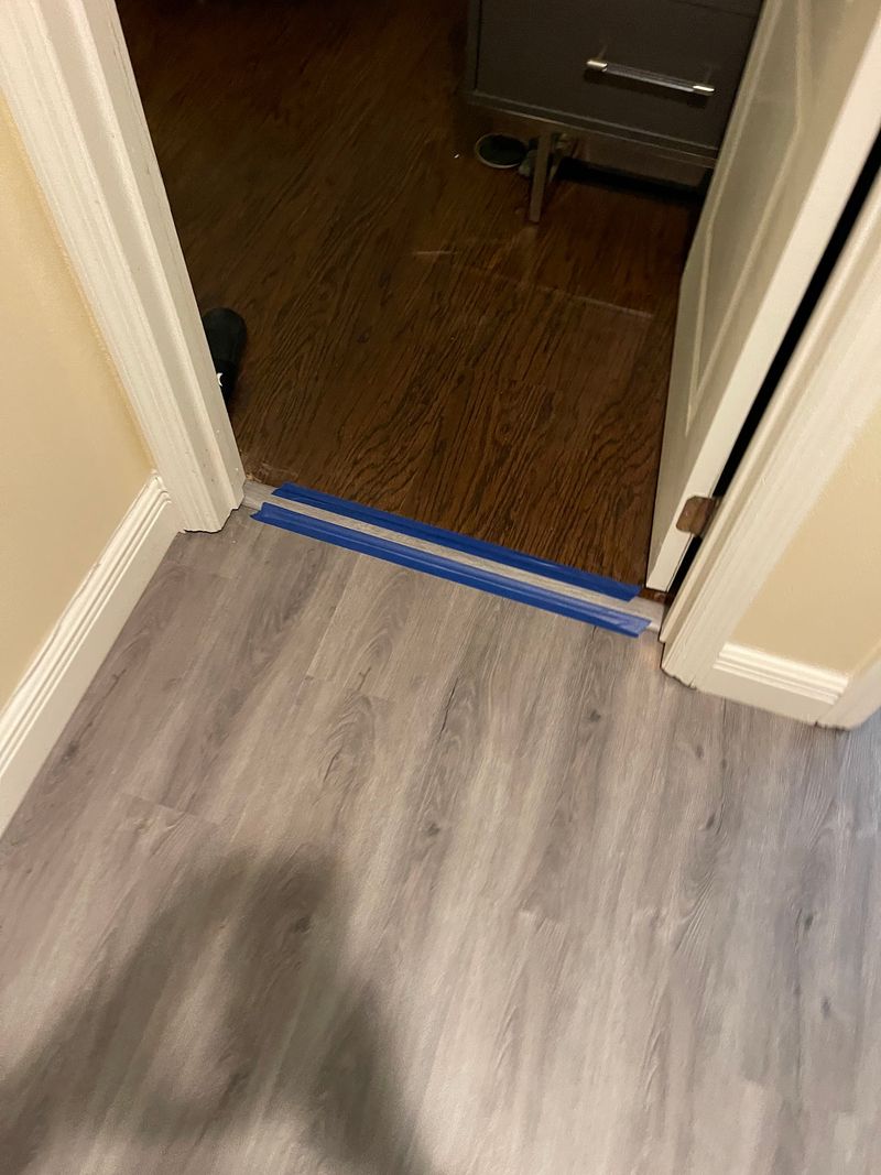 Doorway transition from gray vinyl plank hallway to a dark bedroom floor