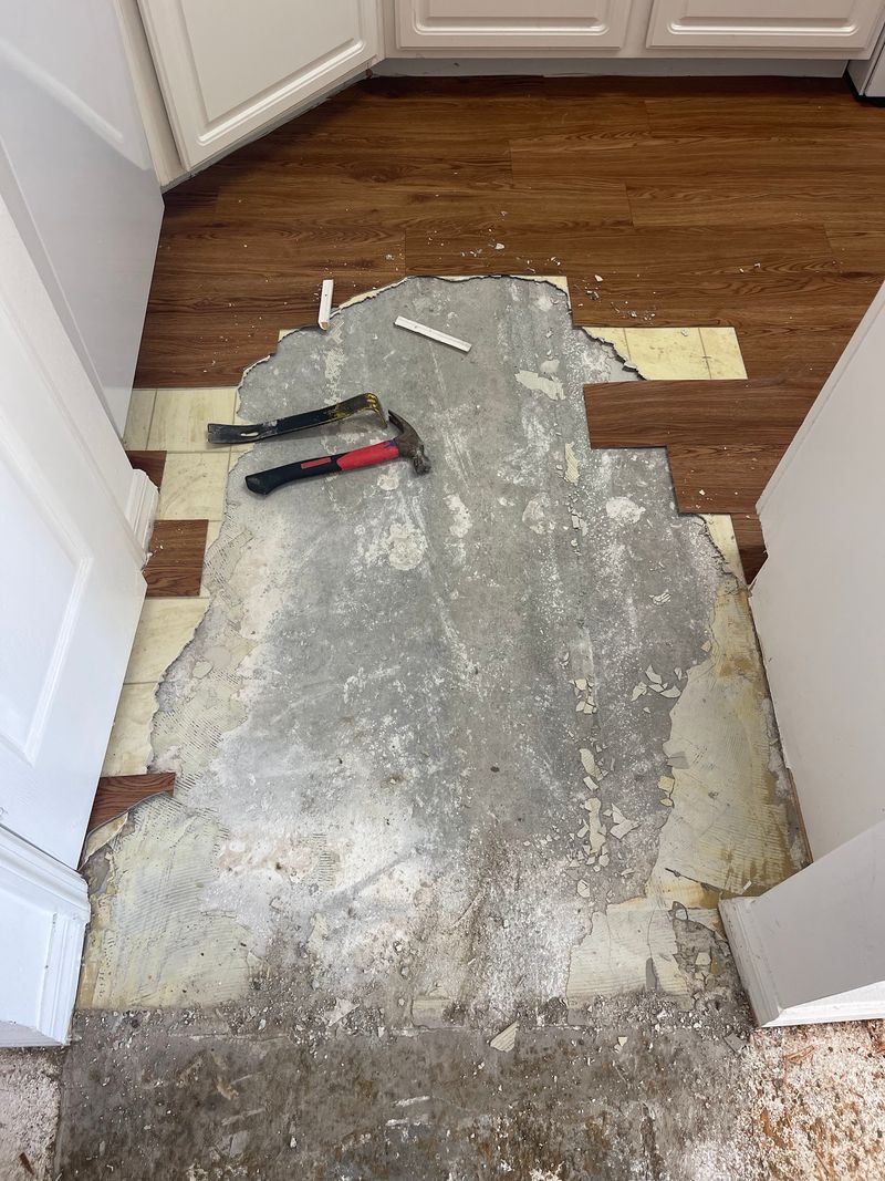 Old flooring layers torn out down to the slab beside white cabinets