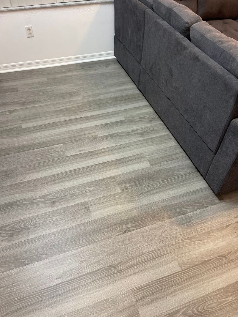 Gray wood-look vinyl plank flooring beside a dark sectional sofa