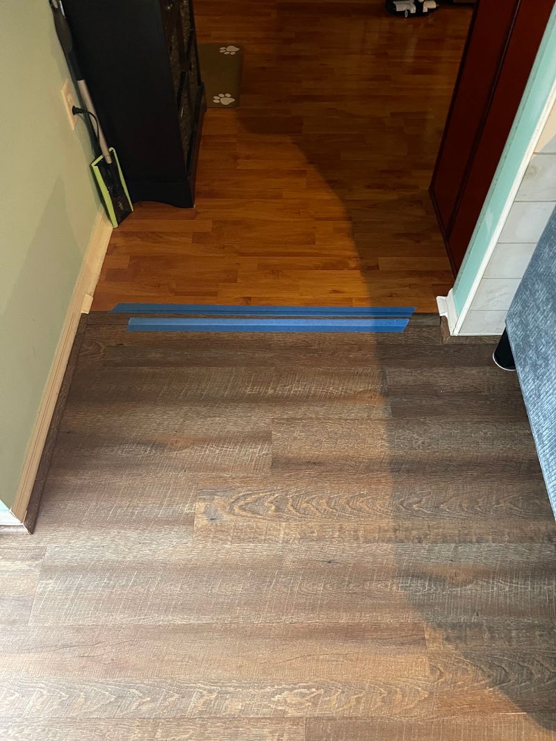 Doorway transition from new dark vinyl plank to an adjacent reddish floor