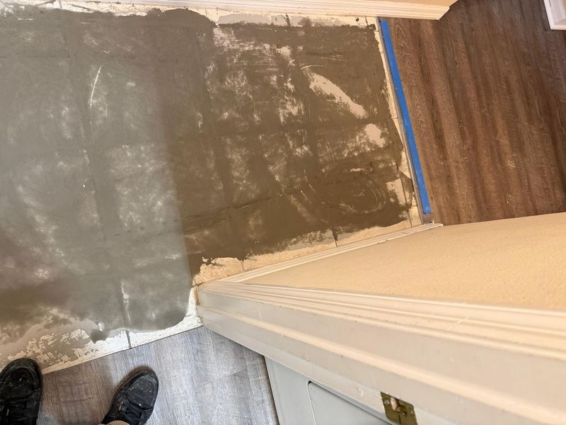 Leveling compound spread over the old floor area beside new gray plank