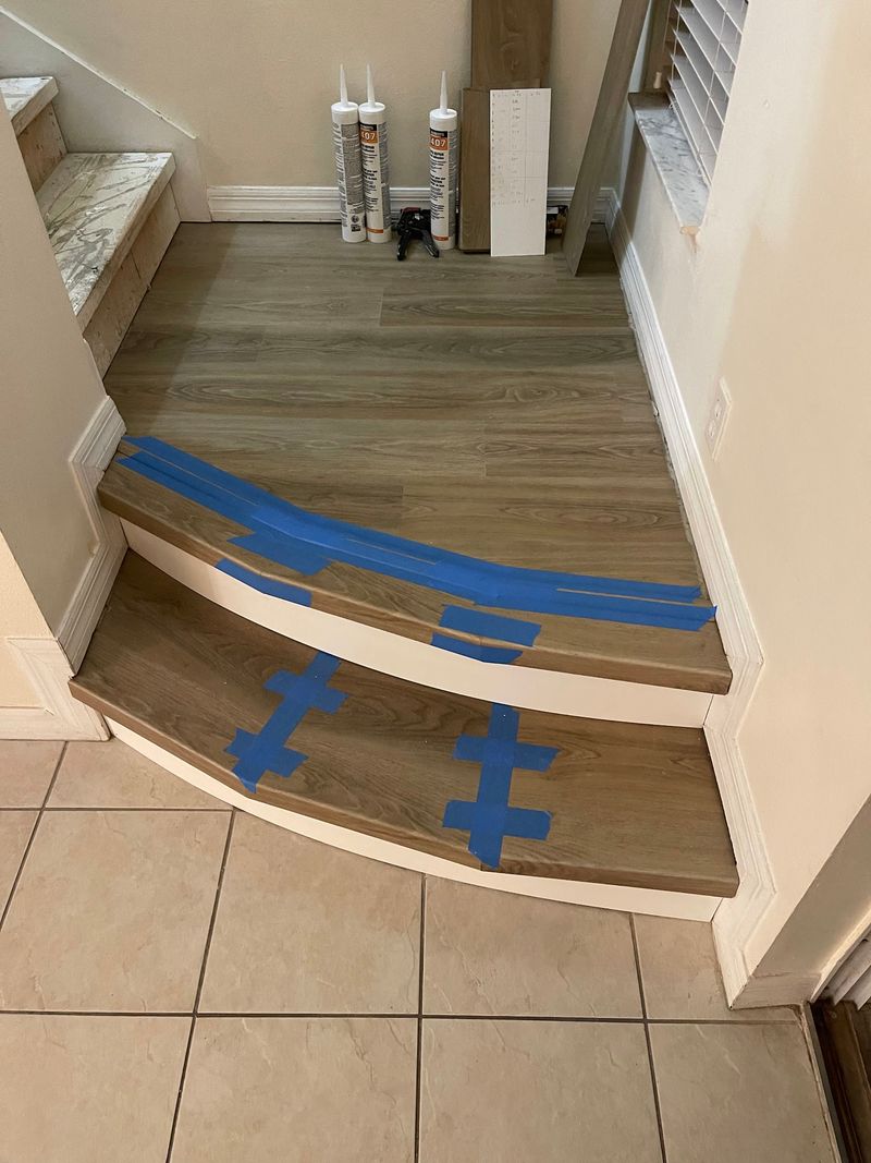 New vinyl plank treads on the lower steps held with blue tape while setting