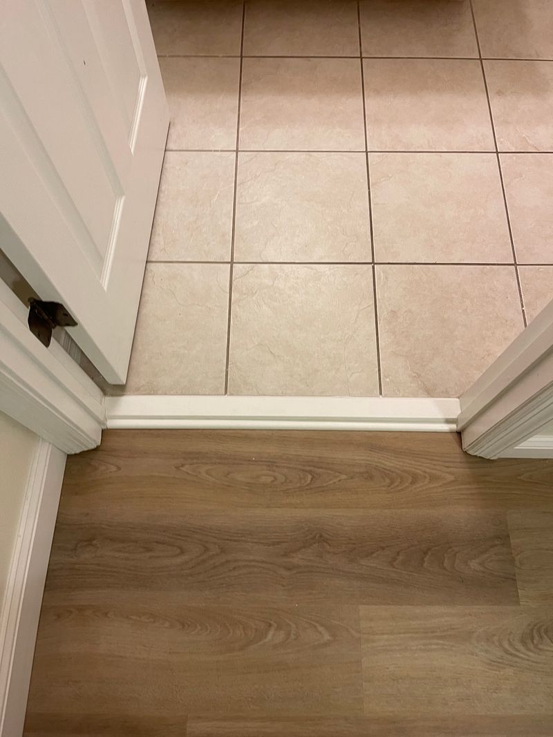 Doorway transition from beige tile to gray-brown vinyl plank flooring