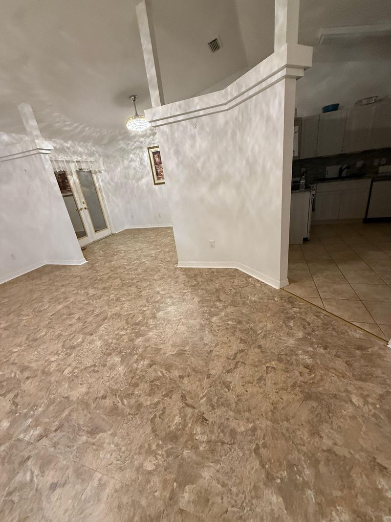 Open area with beige vinyl floor running past a half wall toward the kitchen