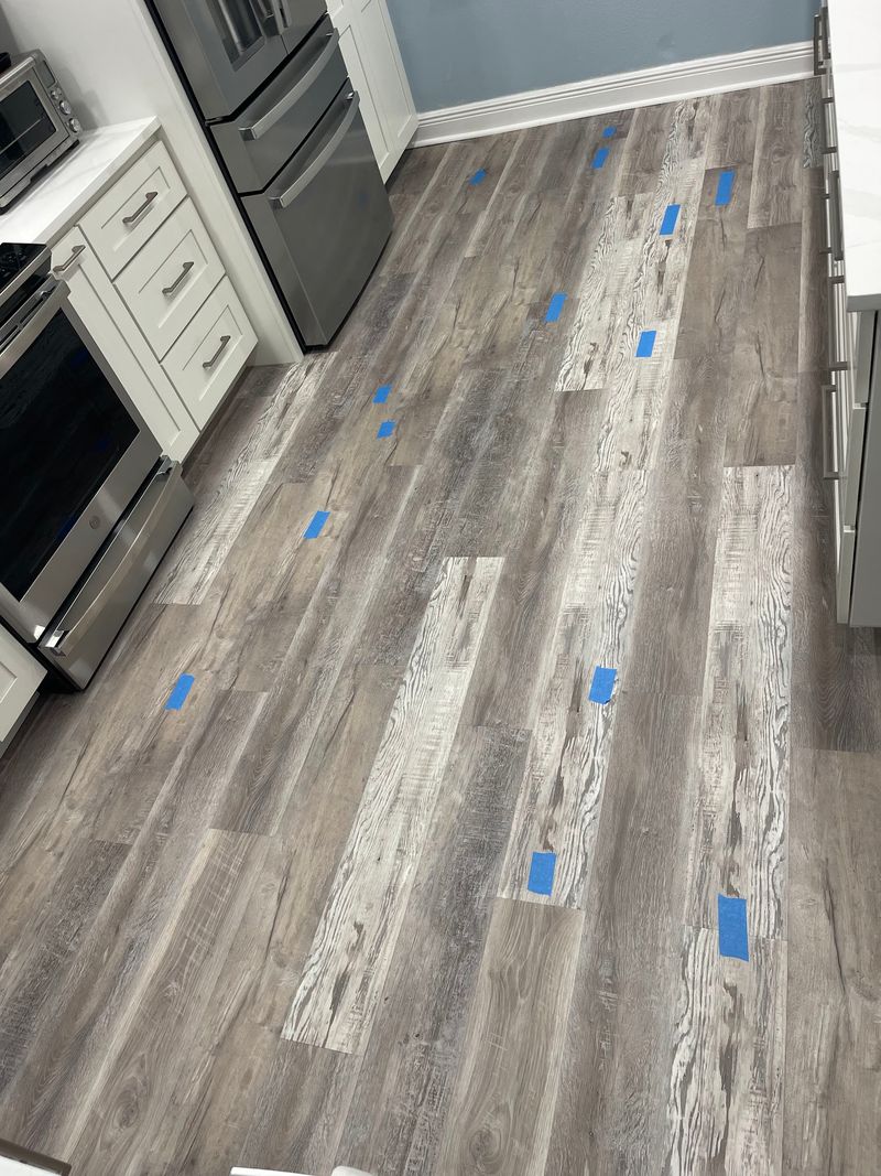 Kitchen with old gray plank floor, problem boards marked with blue tape