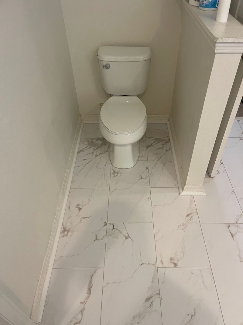 Toilet alcove with white stone-look vinyl flooring and white baseboards
